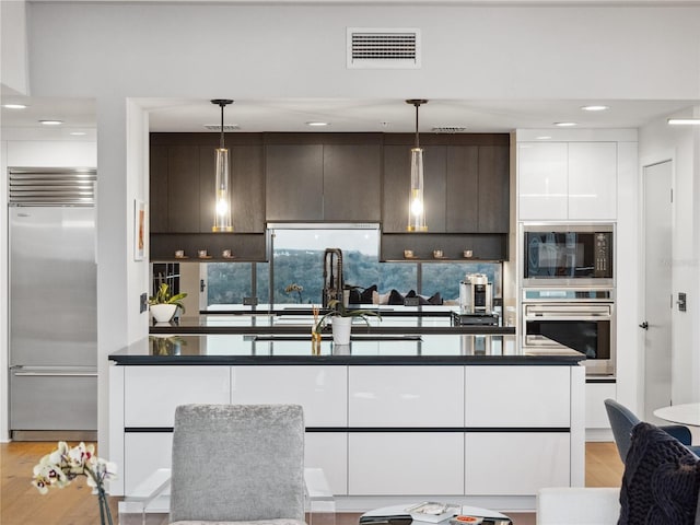 kitchen featuring built in appliances, decorative light fixtures, light hardwood / wood-style floors, and white cabinets