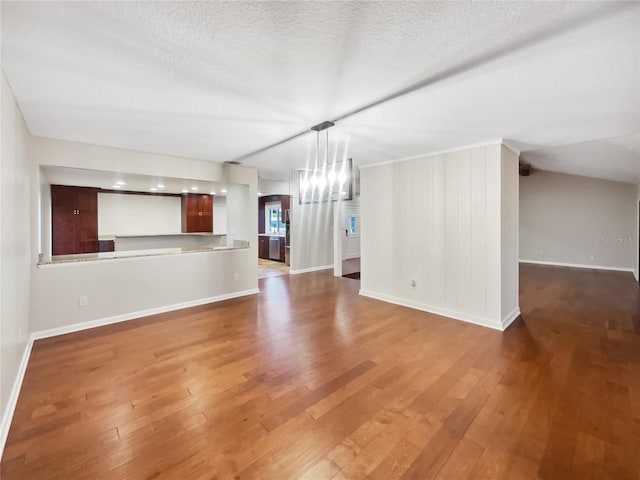 unfurnished living room with an inviting chandelier, a textured ceiling, and hardwood / wood-style floors