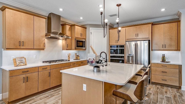 kitchen with pendant lighting, a center island with sink, wall chimney range hood, ornamental molding, and stainless steel appliances