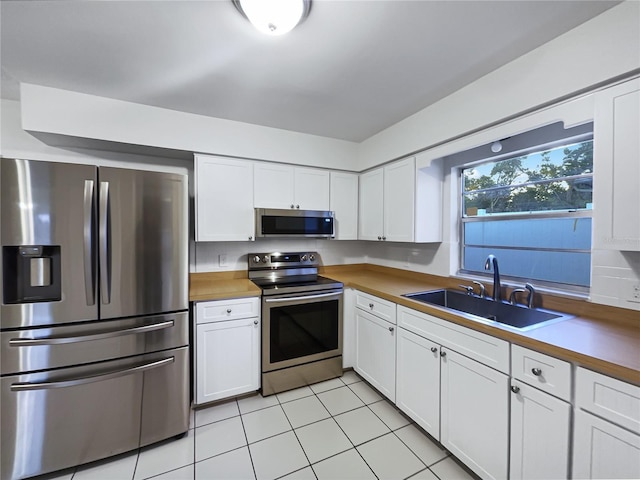 kitchen featuring butcher block counters, white cabinetry, appliances with stainless steel finishes, light tile patterned flooring, and sink