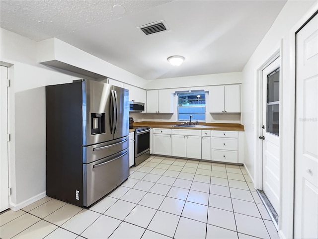 kitchen featuring stainless steel appliances, sink, white cabinetry, a textured ceiling, and light tile patterned flooring