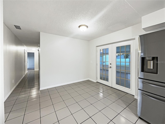 empty room featuring a textured ceiling, french doors, and tile patterned flooring