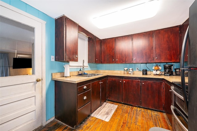 kitchen with sink, stainless steel range with electric cooktop, black fridge, and hardwood / wood-style floors