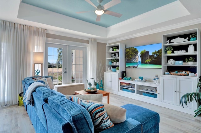 living room with light wood-type flooring, french doors, a tray ceiling, and ceiling fan