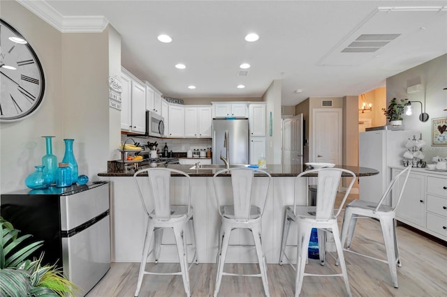 kitchen with white cabinets, appliances with stainless steel finishes, dark stone counters, a kitchen breakfast bar, and kitchen peninsula