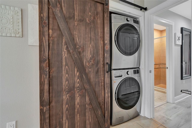 clothes washing area featuring stacked washer / dryer, light tile patterned floors, and a barn door