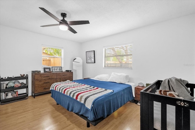 bedroom with a textured ceiling, ceiling fan, light hardwood / wood-style floors, and multiple windows