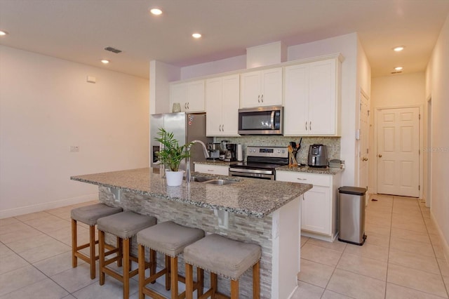 kitchen with light tile patterned floors, a kitchen island with sink, white cabinets, appliances with stainless steel finishes, and sink