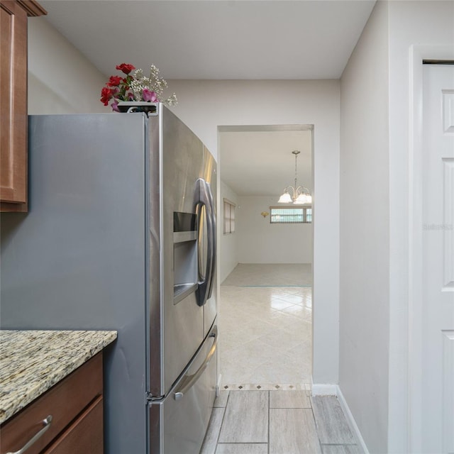 kitchen with stainless steel refrigerator with ice dispenser, a notable chandelier, and light stone countertops