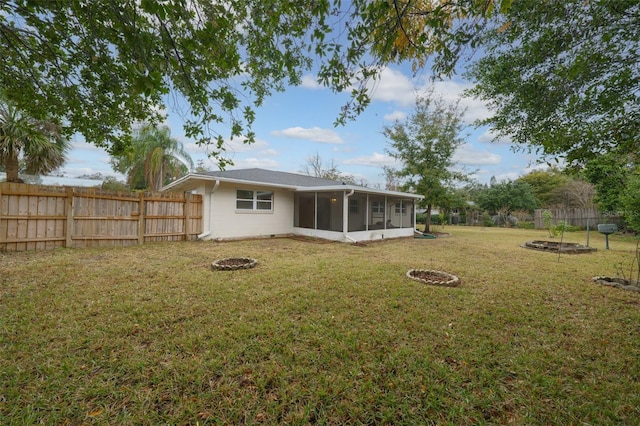 back of house featuring a sunroom, a yard, and a fire pit