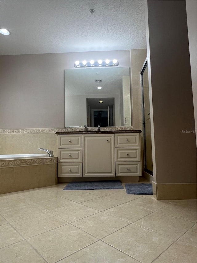 bathroom with a textured ceiling, tile patterned floors, tiled tub, and vanity