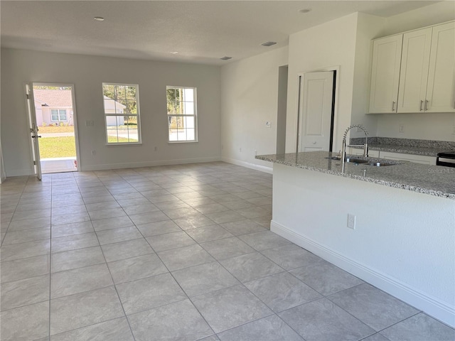 kitchen with sink, white cabinets, light tile patterned floors, and light stone counters