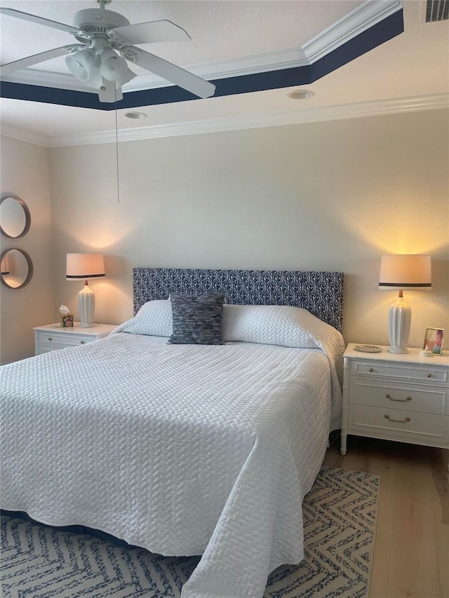 bedroom featuring dark wood-style flooring, a ceiling fan, visible vents, a raised ceiling, and crown molding