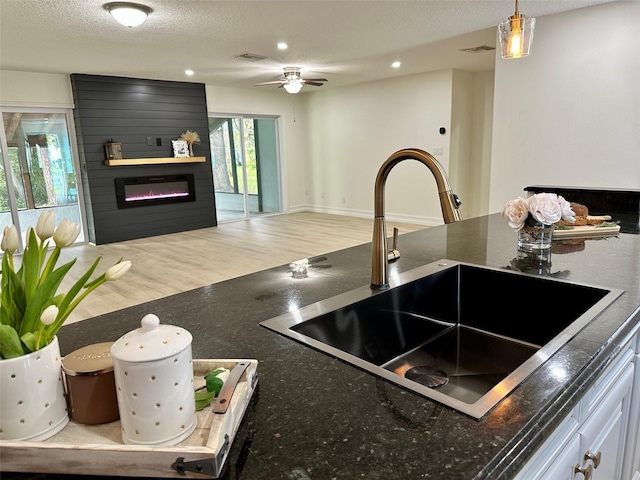 kitchen with sink, white cabinetry, a textured ceiling, a large fireplace, and hanging light fixtures