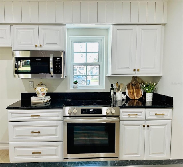 kitchen with white cabinets, hardwood / wood-style floors, dark stone counters, and appliances with stainless steel finishes