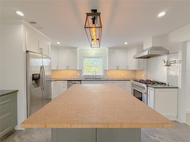 kitchen with appliances with stainless steel finishes, sink, wall chimney range hood, decorative light fixtures, and white cabinets