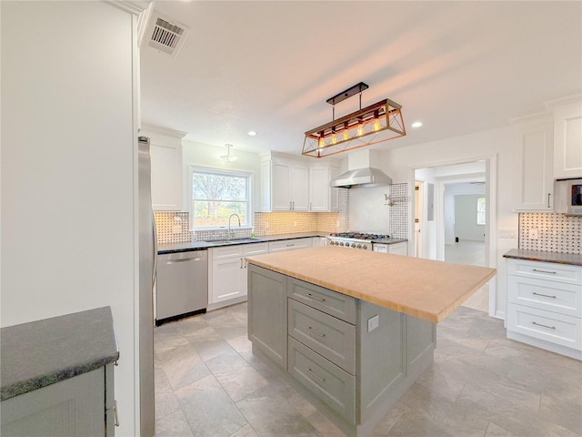 kitchen with stainless steel appliances, a kitchen island, sink, wall chimney range hood, and white cabinetry