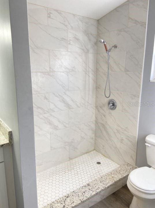 bathroom featuring a tile shower, hardwood / wood-style flooring, toilet, and vanity