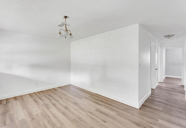 unfurnished room with a textured ceiling, light hardwood / wood-style flooring, and an inviting chandelier