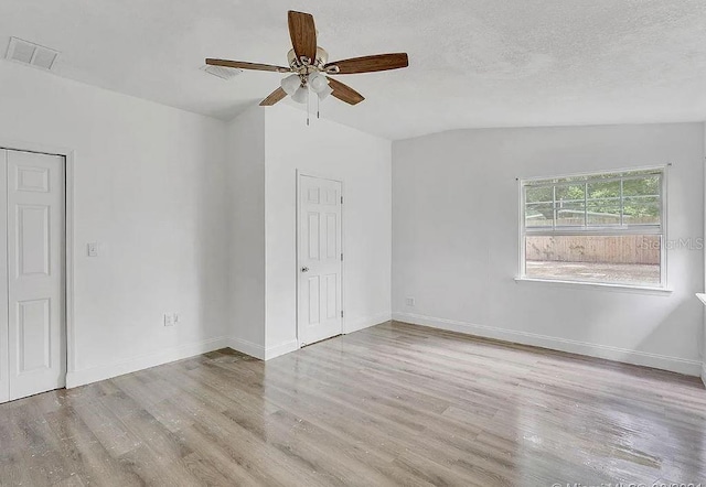 empty room featuring light hardwood / wood-style floors, a textured ceiling, lofted ceiling, and ceiling fan