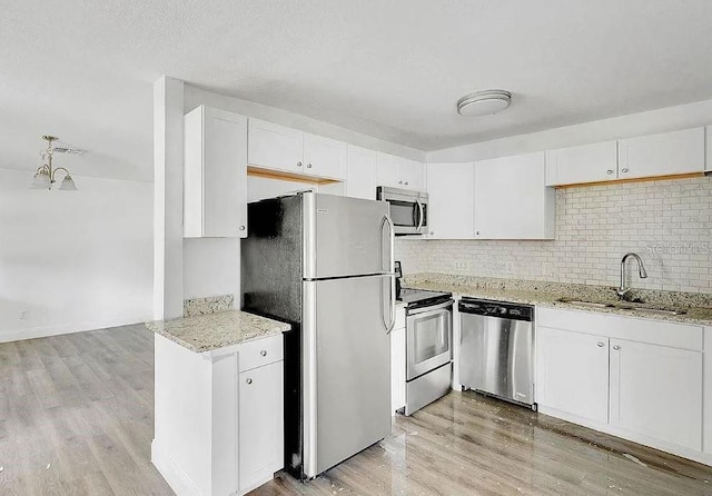 kitchen with appliances with stainless steel finishes, white cabinetry, sink, light hardwood / wood-style flooring, and light stone counters