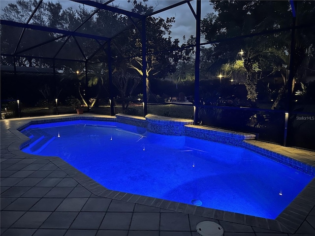 pool at dusk featuring a lanai and a patio