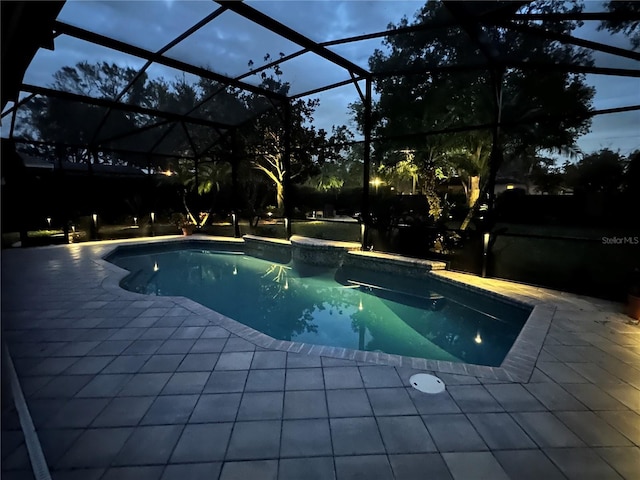 pool at dusk featuring glass enclosure and a patio area