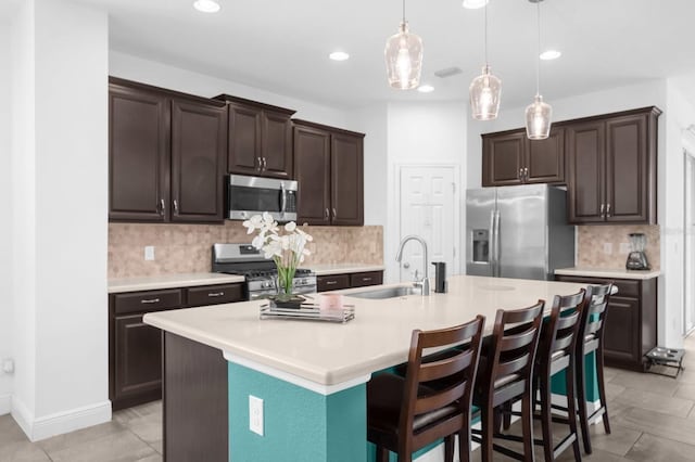 kitchen with dark brown cabinets, a center island with sink, stainless steel appliances, and a breakfast bar