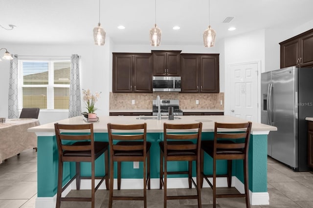 kitchen with stainless steel appliances, a center island with sink, and decorative light fixtures