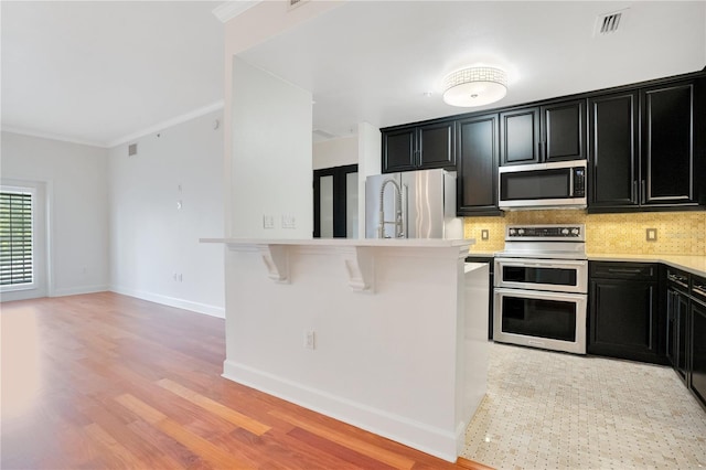 630 Vassar St Unit 2310, Orlando, FL 32804 - kitchen with crown molding, light wood-type flooring, a kitchen breakfast bar, stainless steel appliances, and backsplash