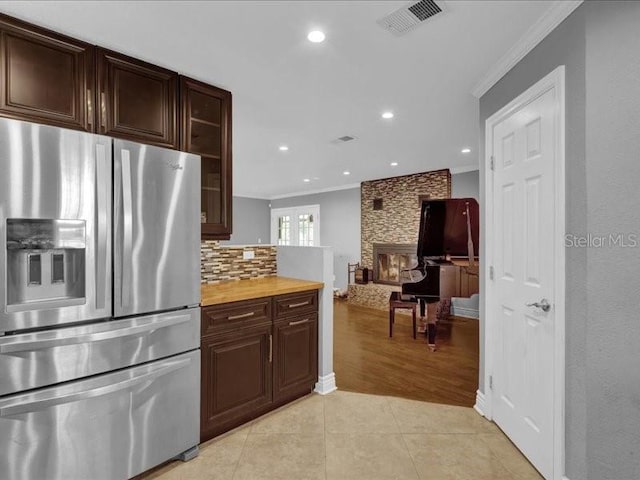 kitchen with stainless steel fridge, backsplash, a fireplace, ornamental molding, and light tile patterned flooring