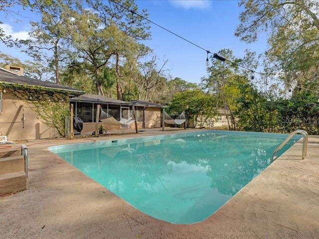 view of swimming pool featuring a sunroom and a patio