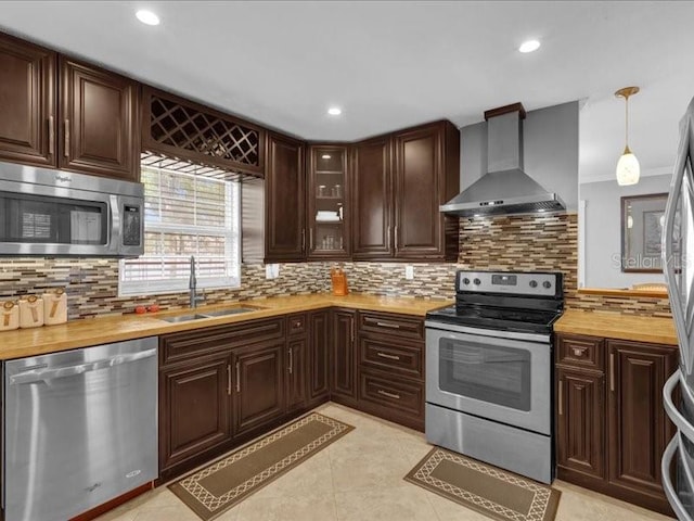 kitchen featuring butcher block counters, sink, appliances with stainless steel finishes, pendant lighting, and wall chimney range hood