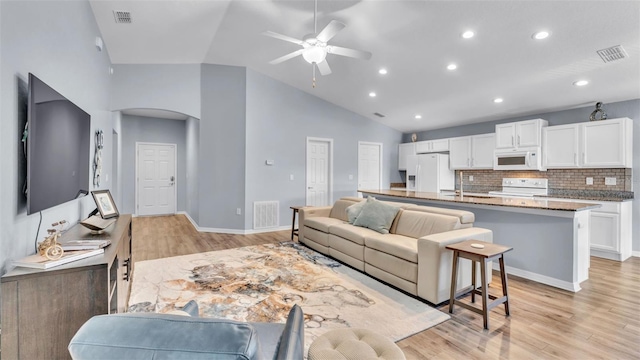 living room with ceiling fan, light hardwood / wood-style floors, high vaulted ceiling, and sink