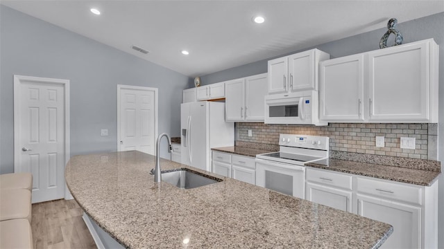 kitchen with lofted ceiling, a center island with sink, sink, white appliances, and white cabinets