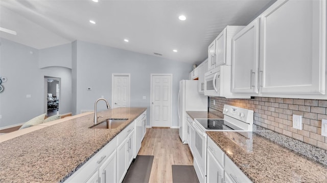 kitchen featuring white appliances, light stone countertops, vaulted ceiling, white cabinets, and sink