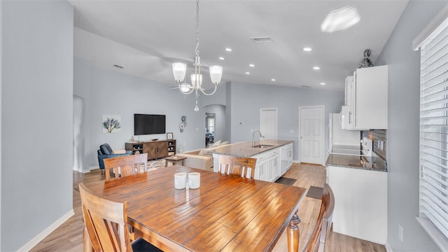 dining room with light hardwood / wood-style floors, sink, a notable chandelier, and vaulted ceiling