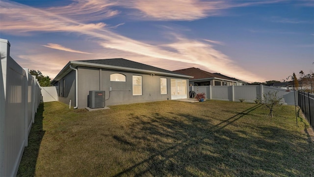 back house at dusk featuring a yard and central AC