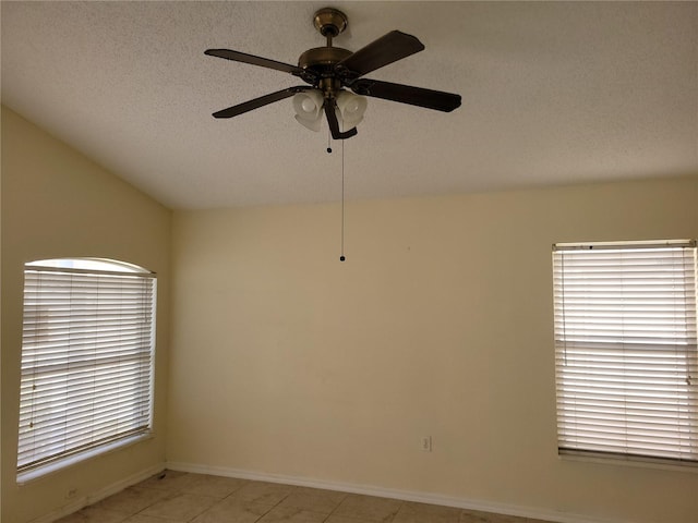 empty room with a textured ceiling, ceiling fan, light tile patterned flooring, and vaulted ceiling