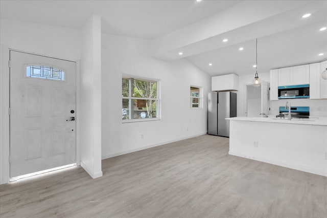 kitchen with pendant lighting, lofted ceiling, white cabinets, appliances with stainless steel finishes, and light hardwood / wood-style floors