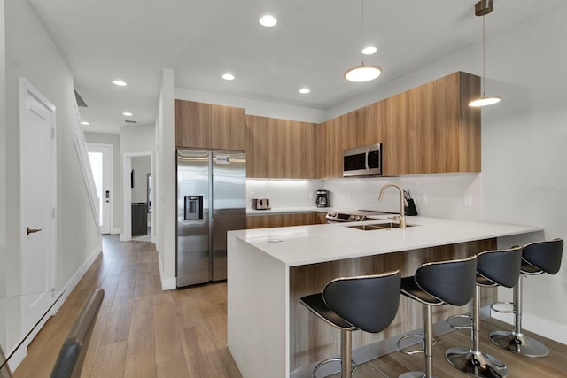 kitchen with pendant lighting, sink, light wood-type flooring, kitchen peninsula, and stainless steel appliances