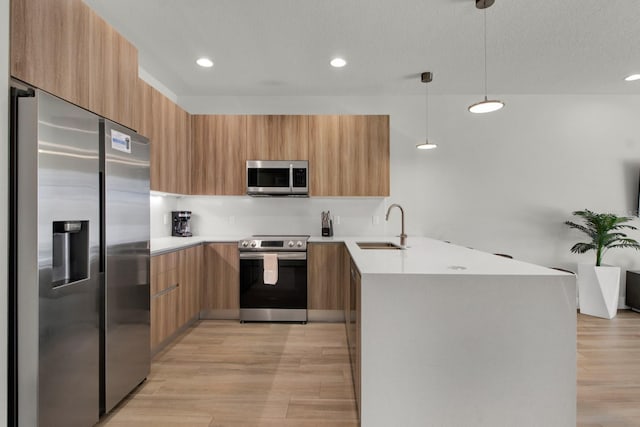 kitchen featuring sink, hanging light fixtures, light wood-type flooring, kitchen peninsula, and stainless steel appliances