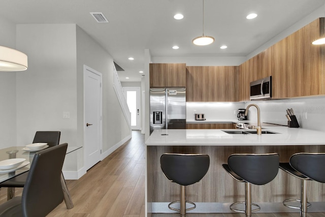 kitchen featuring sink, stainless steel appliances, kitchen peninsula, a breakfast bar area, and light wood-type flooring