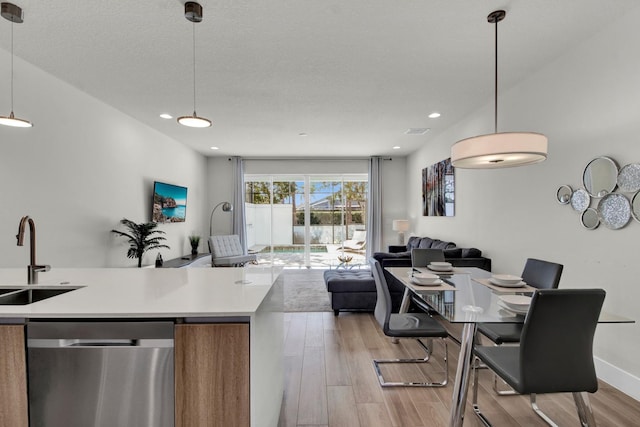 kitchen with pendant lighting, sink, stainless steel dishwasher, a textured ceiling, and light hardwood / wood-style floors