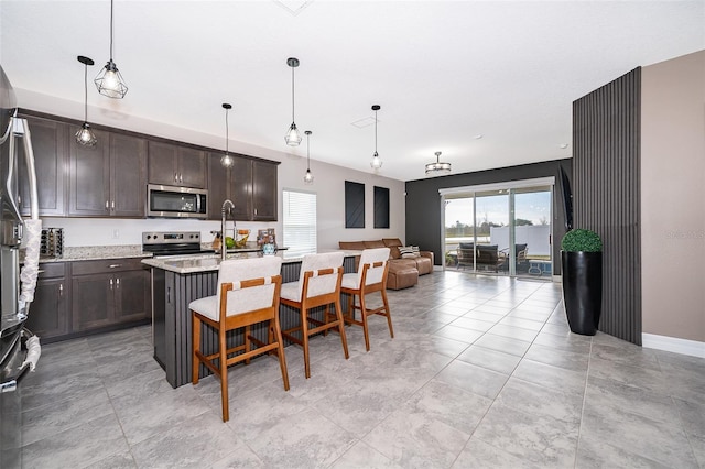 kitchen featuring dark brown cabinets, pendant lighting, an island with sink, and appliances with stainless steel finishes