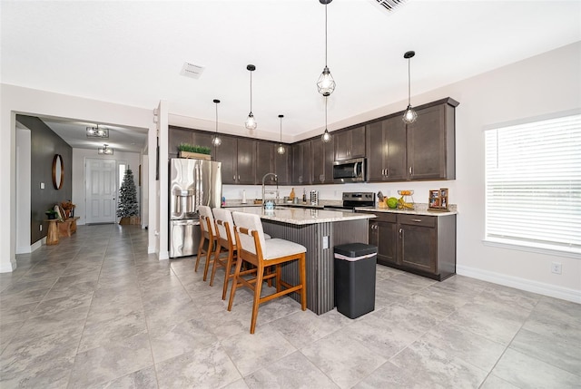 kitchen with pendant lighting, an island with sink, appliances with stainless steel finishes, a kitchen breakfast bar, and dark brown cabinetry