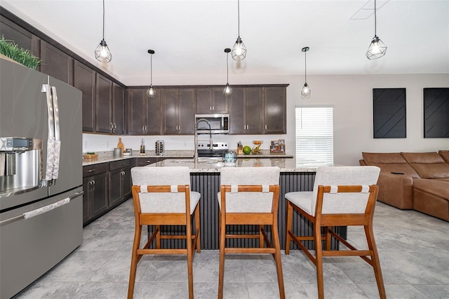 kitchen with a center island with sink, decorative light fixtures, dark brown cabinets, and appliances with stainless steel finishes