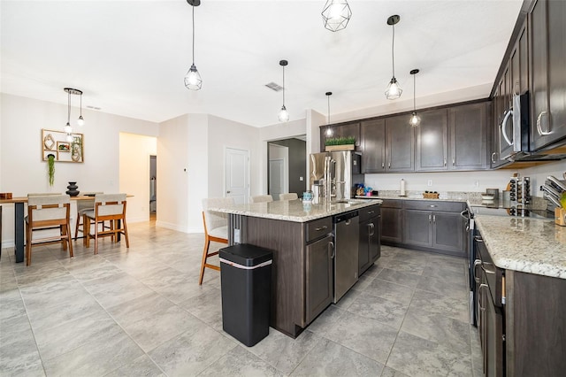 kitchen featuring a center island with sink, decorative light fixtures, dark brown cabinets, and appliances with stainless steel finishes