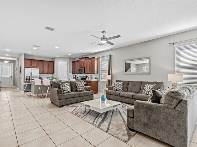 living room with a textured ceiling, ceiling fan, and light tile patterned flooring