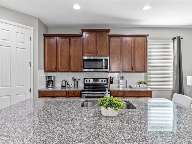 kitchen featuring stainless steel appliances, dark stone counters, backsplash, and a wealth of natural light